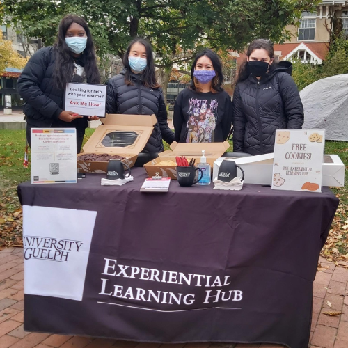 Group of four people wearing masks outside at an Experiential Learning Hub table