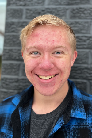 Headshot of person with blonde hair, smiling, wearing a blue and black plaid shirt.