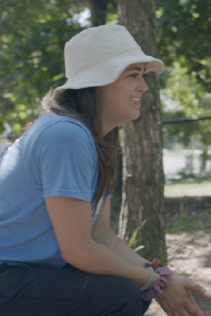 Side profile of a person wearing a white bucket hat and blue tshirt, smiling outside.
